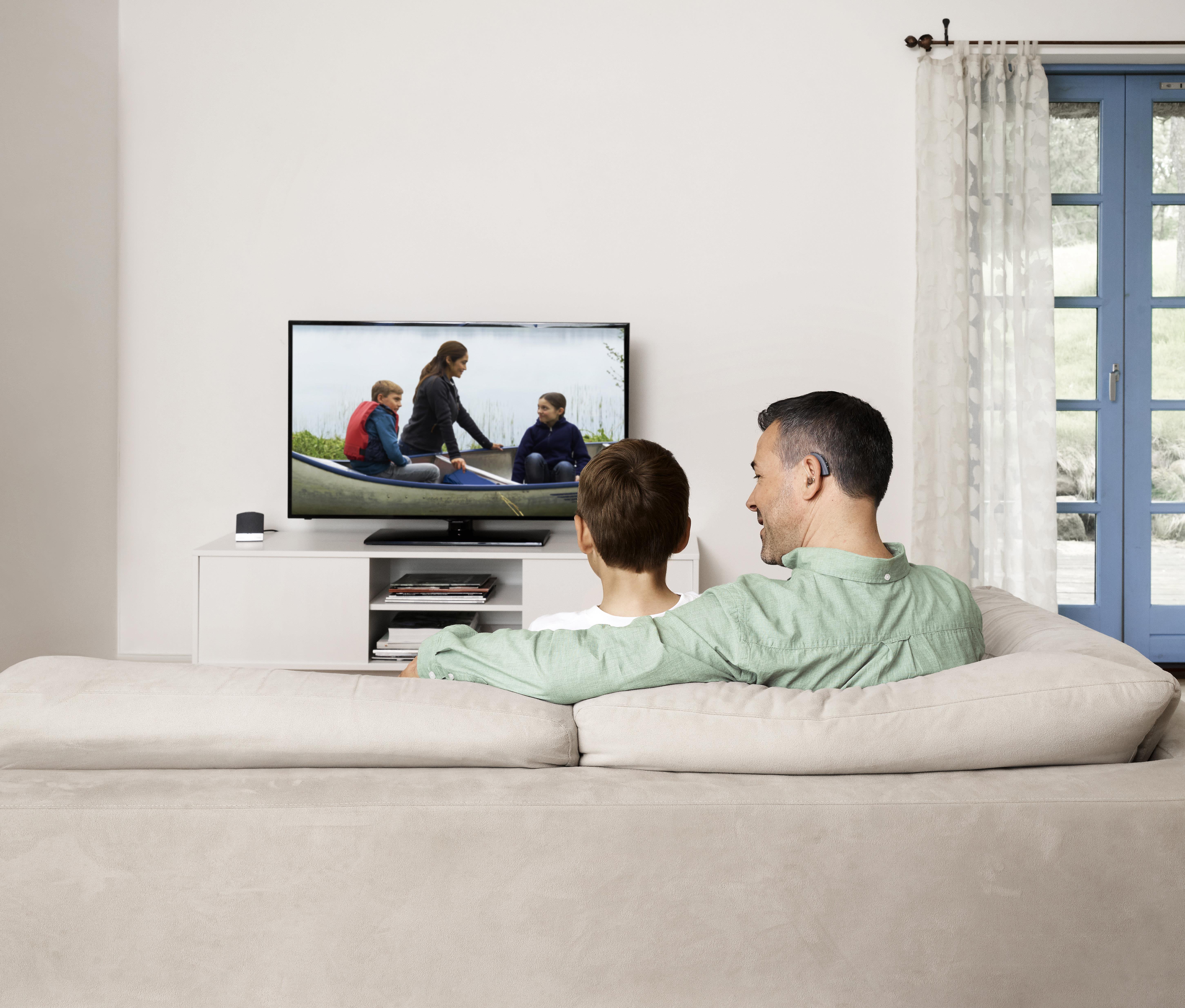 Hombre utilizando un audífono Beltone Boost Max y viendo la televisión con su hijo.