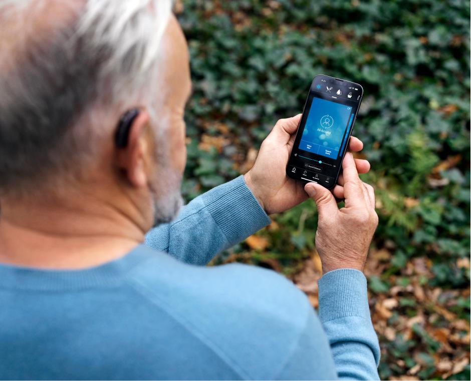 Uono con apparecchi acustici BTE che utilizza l'app Beltone HearMax sul suo smartphone