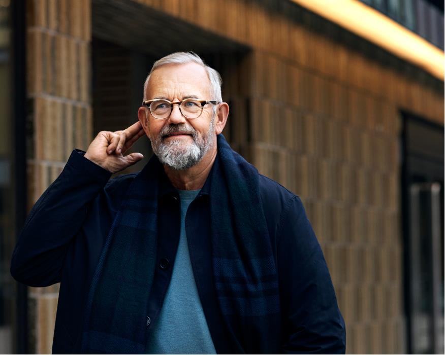 Man with glasses pushing a button on his hearing aid