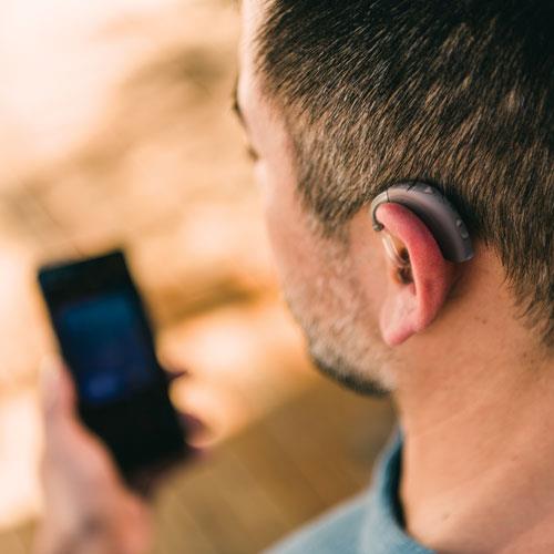 Uomo che tiene in mano un iPhone di Apple e controlla i suoi apparecchi acustici.