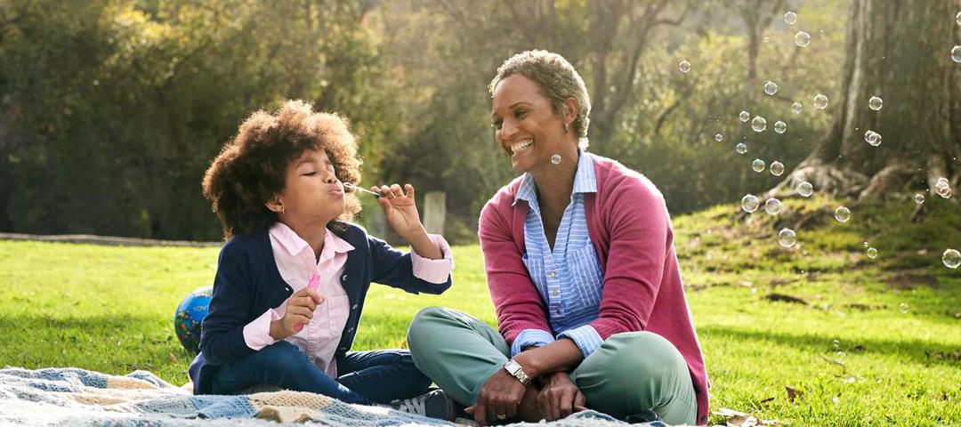 woman and child sitting in a park blowing bubbles